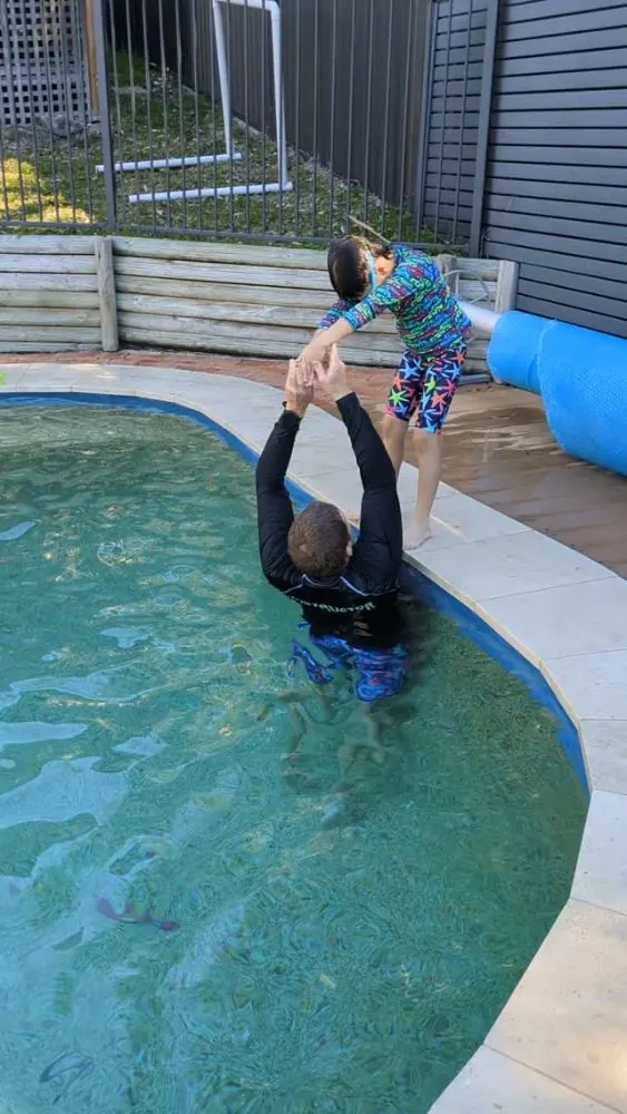 Coach lifting a child for a jump into the pool