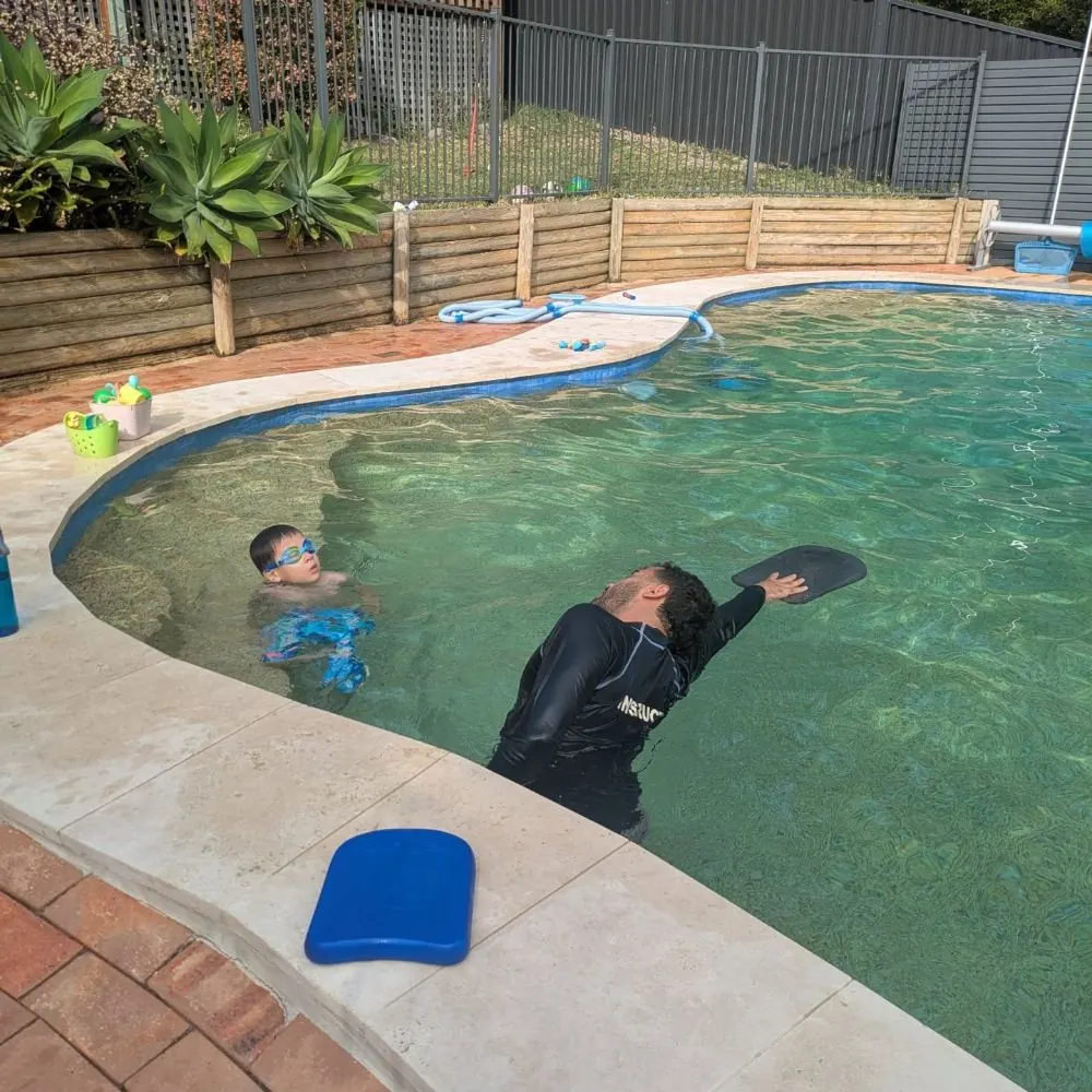 Coach teaching a private lesson in a sunny backyard pool
